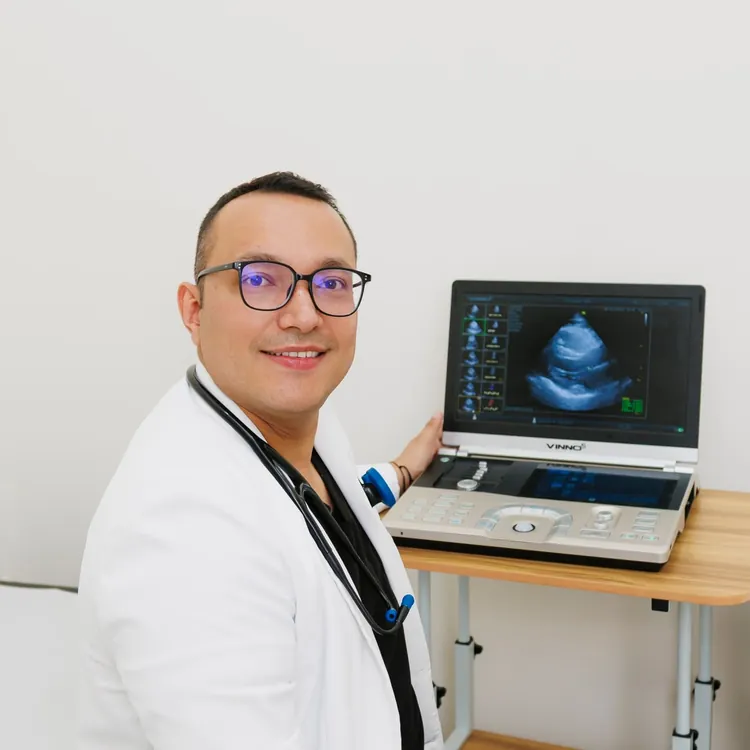 Dr. Edgar Lugo Osuna con bata blanca, sentado junto al ecocardiógrafo de su consultorio