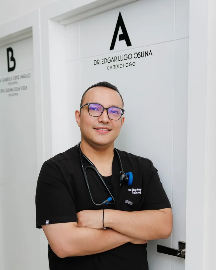 Dr. Edgar Lugo Osuna con uniforme negro y estetoscopio, frente a la puerta de su consultorio en Nogales